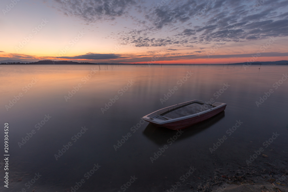Naklejka premium A little fishing boat in the middle of perfectly still water at 