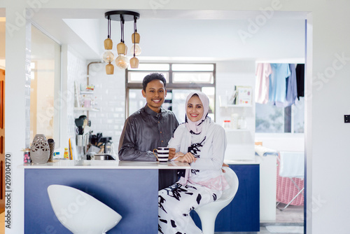 Tableau sur toile A young Muslim Malay couple sit at a table top counter and enjoy a coffee early in the morning when they break fast
