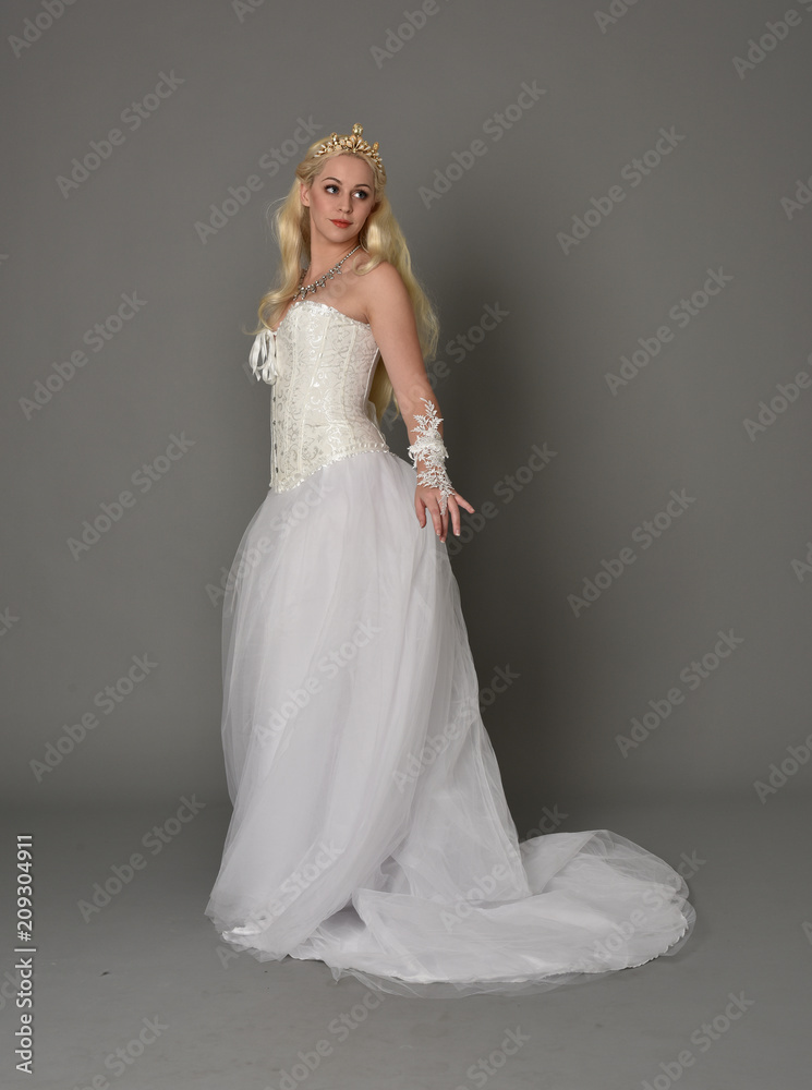 full length portrait of blonde girl wearing white corset gown. standing pose on grey studio background.