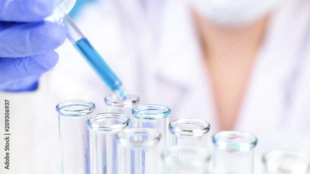 Close up of pipette with liquid blue water drop intro glass test tube in laboratory. Close up of pipette with liquid blue water drop intro glass test tube in laboratory.