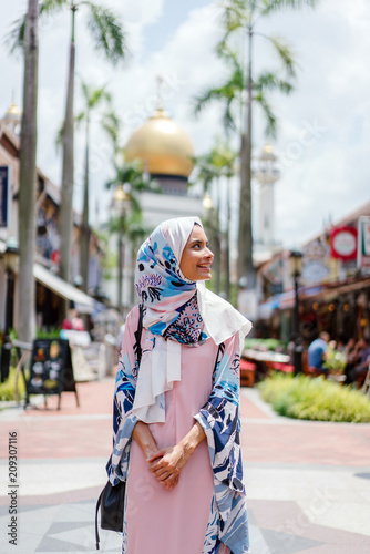 Image of a young and dynamic Muslim woman visiting a Muslim place in Singapore. She enjoys walking around the city while wearing her Abaya dress and head scarves.