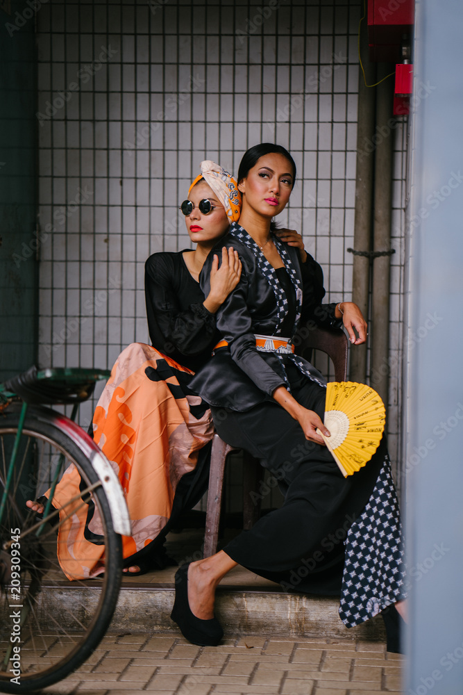 Naklejka premium Portrait of two young, attractive and beautiful Muslim Malay women on a street in Asia during the day. They are dressed up to go visiting for Raya and look fashionable and beautiful. 