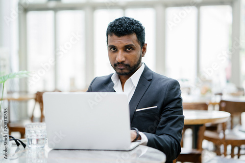 Portrait of an Indian man in a 3-piece suit working on his notebook computer during the day.
