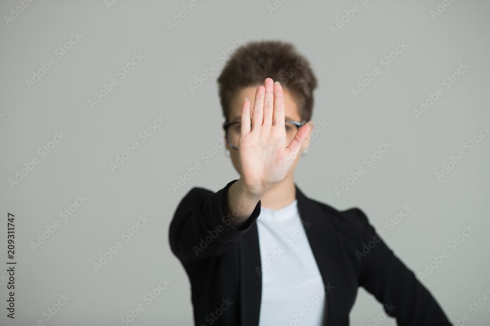 young beautiful girl in a black jacket with a short haircut on a gray background with a serious facial expression and with a gesture of the hand young beautiful girl in a black jacket with a short haircut on a gray background with a serious facial expression and with a gesture of the hand
