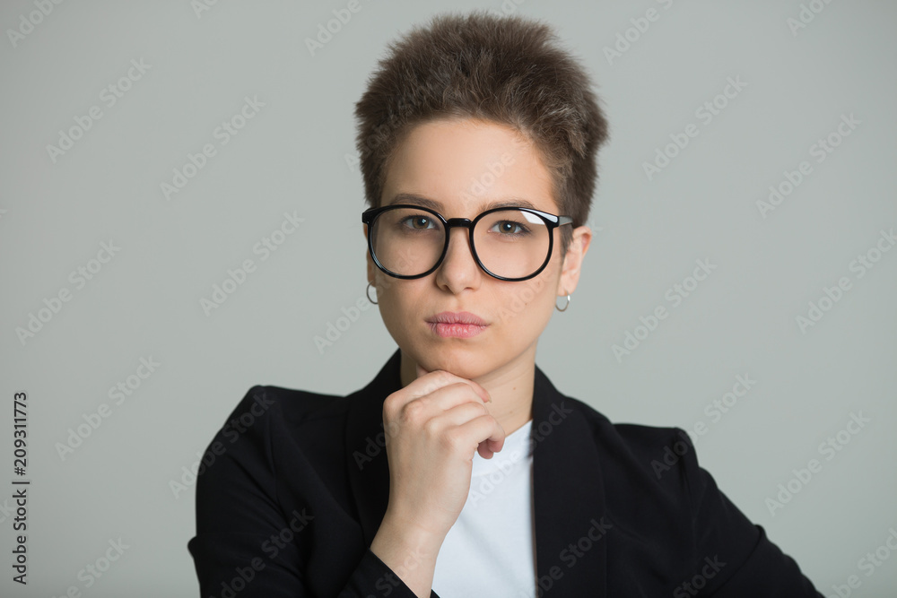 young beautiful girl in a black jacket with a short haircut on a gray background with a serious facial expression young beautiful girl in a black jacket with a short haircut on a gray background with a serious facial expression