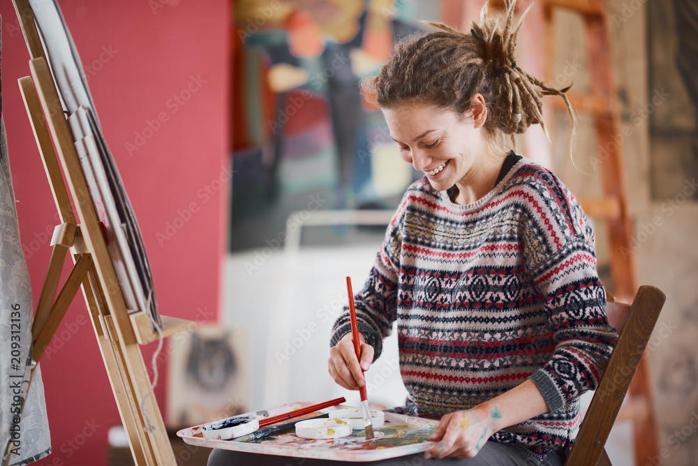 Fototapeta premium Artistic girl sitting in studio and paint on easel.