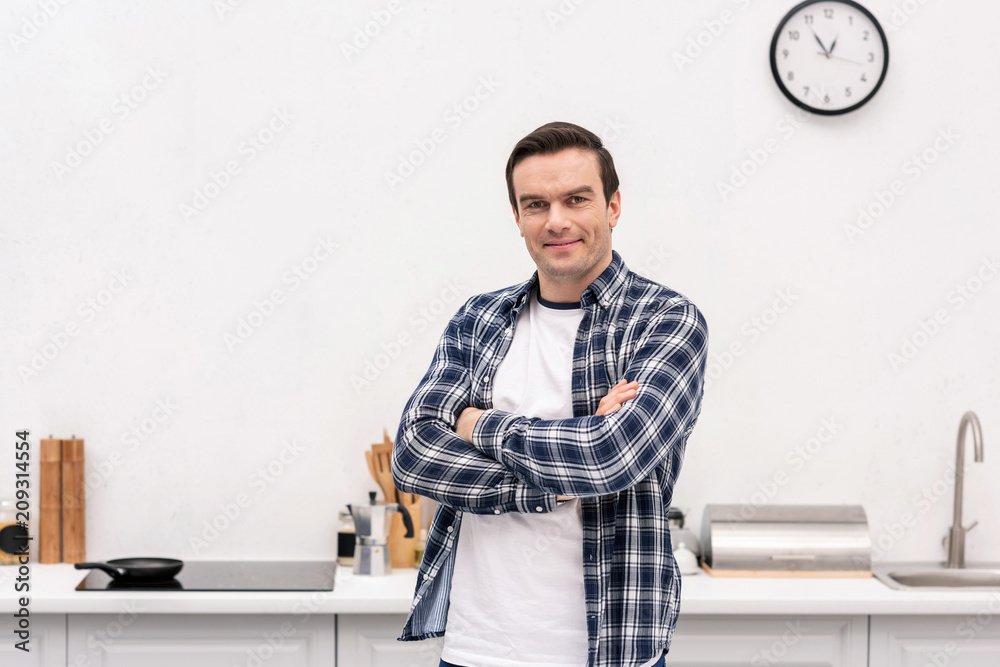 happy adult man with crossed arms at kitchen looking at camera