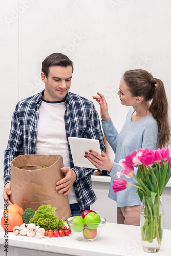 happy adult couple checking buys list in tablet after grocery shopping