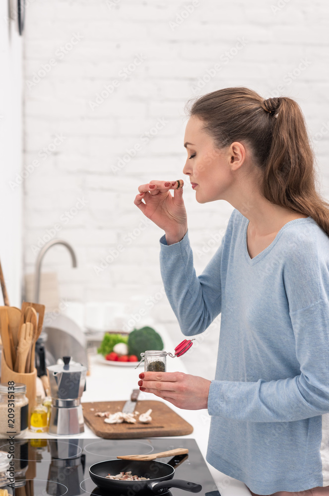 beautiful adult woman sniffing spices over food cooking in frying pan at kitchen beautiful adult woman sniffing spices over food cooking in frying pan at kitchen