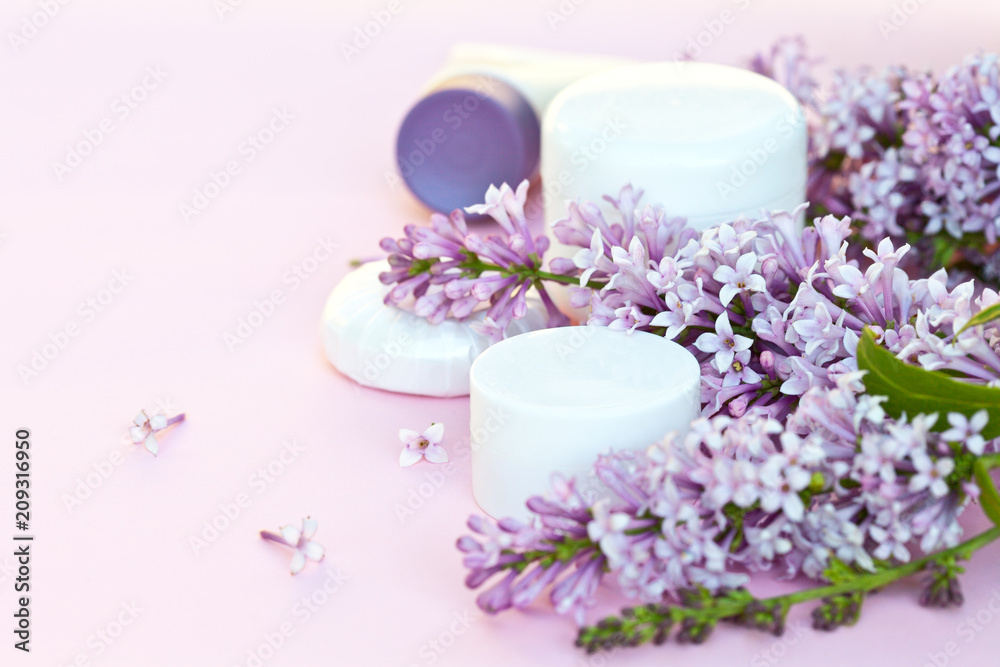Natural floral fragrance cosmetics and spring blooming lilac. Jars with a rejuvenating cream and moisturizing flavored soap on a light pink background. Empty space for text
