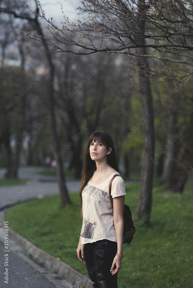 Attractive young woman outside the park . Caucasian girl with long brown hair thoughtful in a serene pose Attractive young woman outside the park . Caucasian girl with long brown hair thoughtful in a serene pose