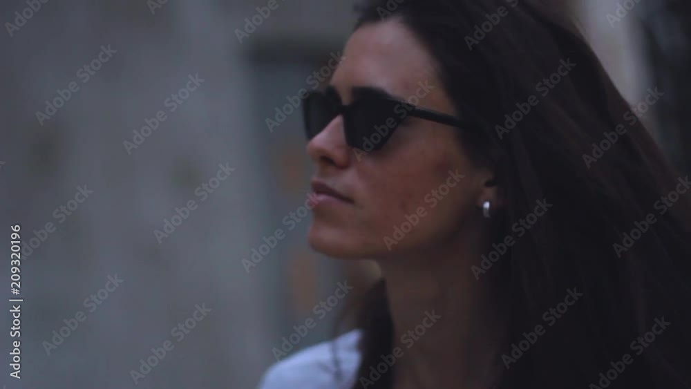 brunette woman is walking in black sunglasses and fixed her hair. she is talking and smiling brunette woman is walking in black sunglasses and fixed her hair. she is talking and smiling
