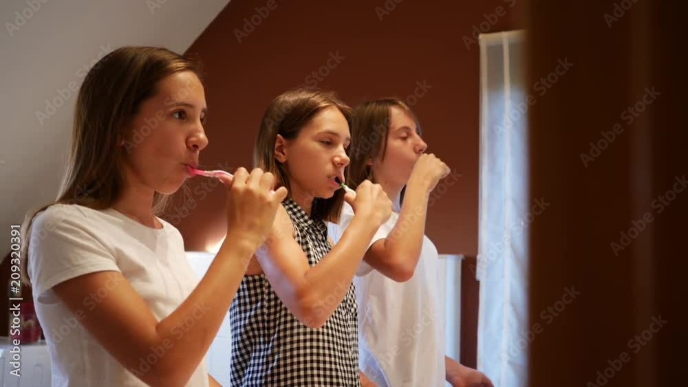Brush teeth in front of the bathroom mirror three girls teenager sisters before going to bed