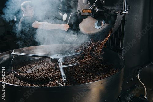 Professional male roaster loading machine with coffee beans photo