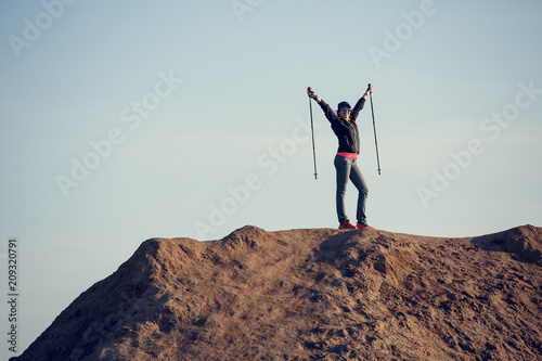 Full-length photo of woman growing tourist with backpack and walking sticks with her hands up on mountain
