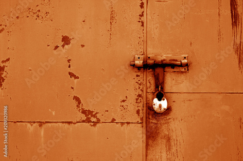 Old padlock on metal gate in orange color.