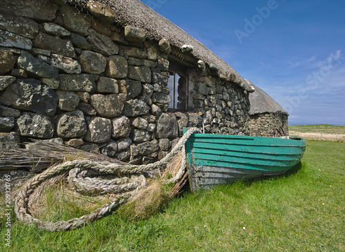 Konstfotografi Isle of Skye, Scotland - Traditional Hebridean blackhouse with thatched roof, wooden fishing boat and coiled rope