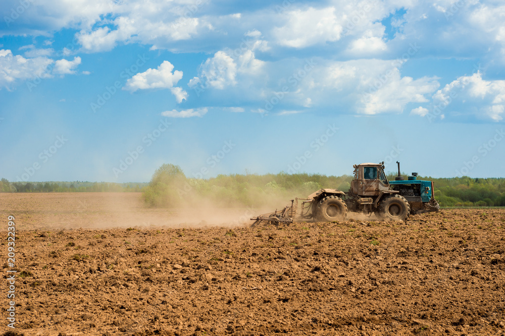 Fototapeta premium Tractor plowing a field on a sunny day. Preparing land for sowing. Agricultural works at farmlands. Tractor ploughing a field with a dust behind it. Agriculture industry