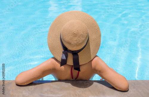 Woman with brown hat relaxing in swimming pool with blue water during a sunny day , holiday concept