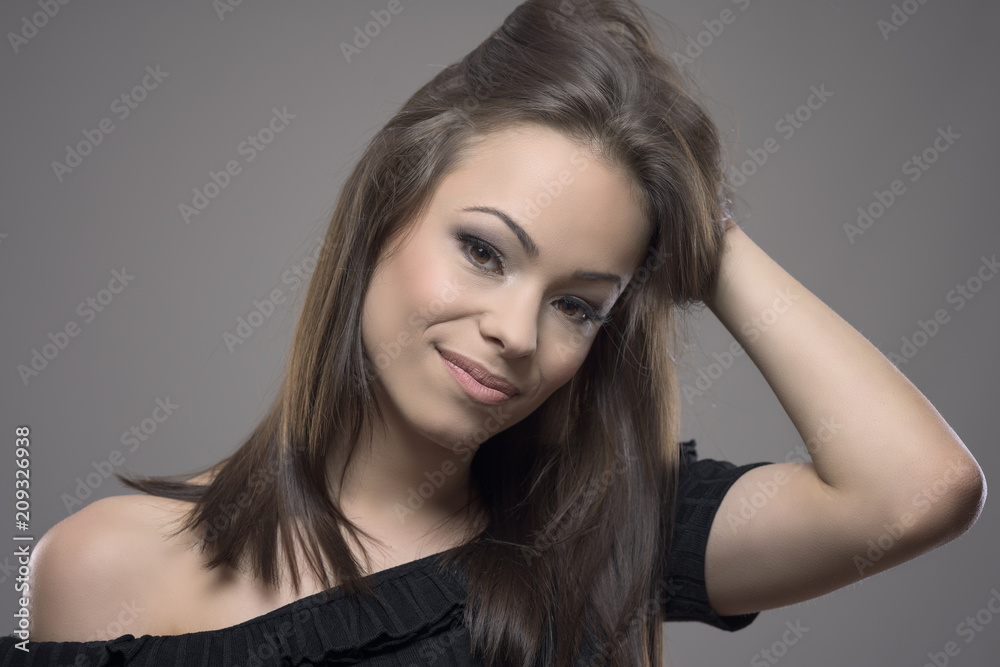 Fototapeta premium Atmospheric moody portrait of gorgeous woman touching hair and looking at camera against gray studio background. 