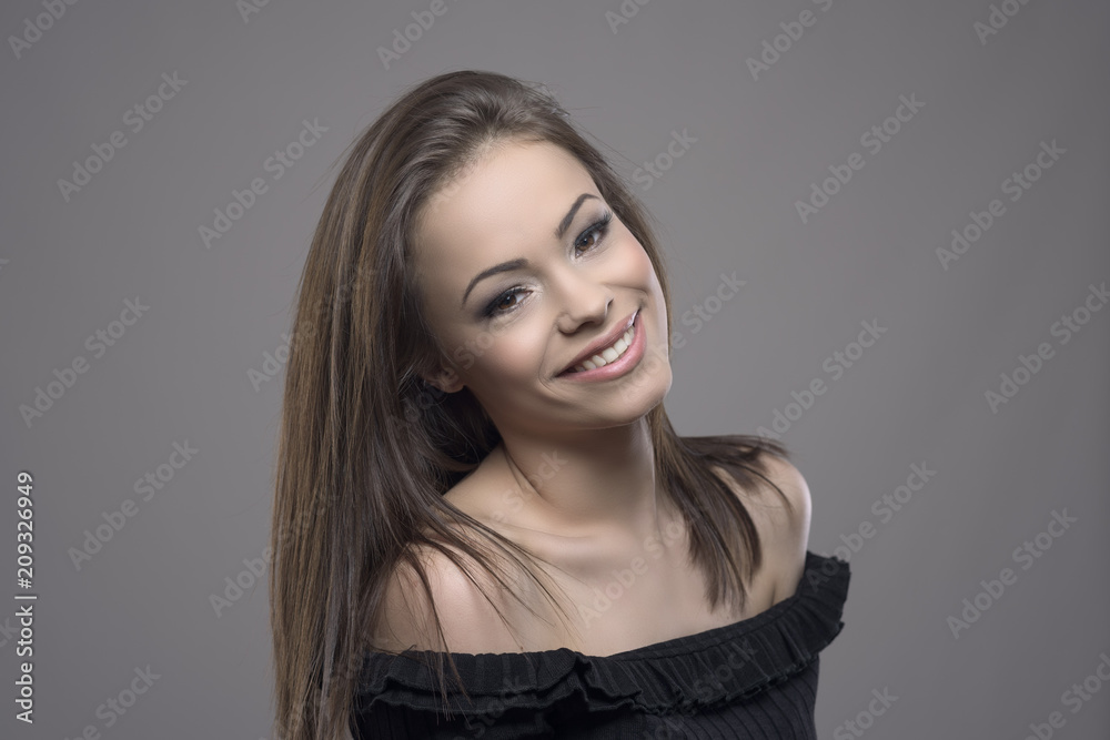 Cute charming young teenage woman with perfect smile looking and smiling at camera against gray studio background. 