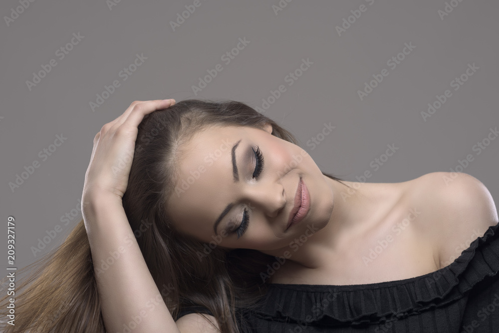 Relaxed pretty young woman brunette touching hair with closed eyes against gray studio background with copyspace. Relaxed pretty young woman brunette touching hair with closed eyes against gray studio background with copyspace.