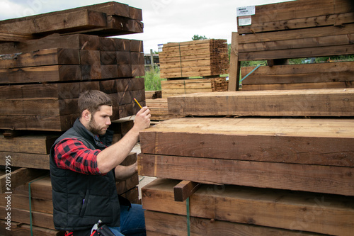 Lumber yard worker, carpenter at wood yard counts inventory with mobile device