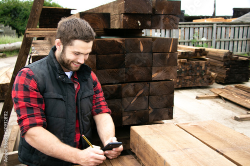 Lumber yard worker, carpenter at wood yard counts inventory with mobile device