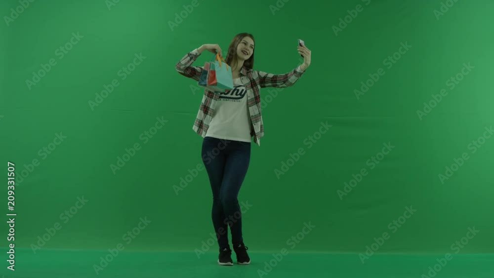 girl with mini bags, standing in a half-turn, looking to the right and taking a selfie on green screen