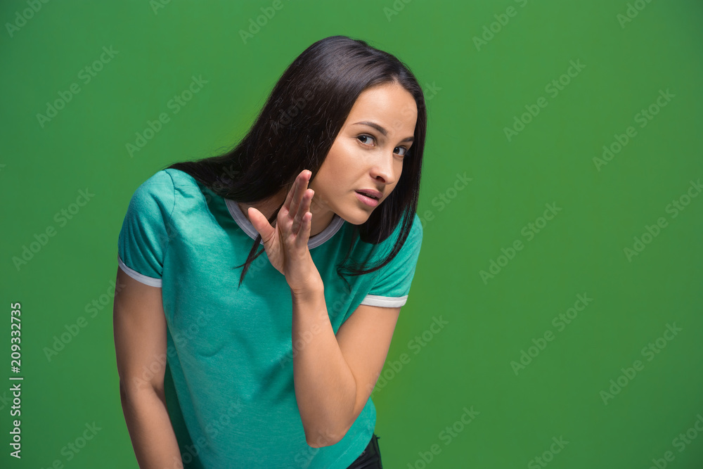 The young woman whispering a secret behind her hand over green background