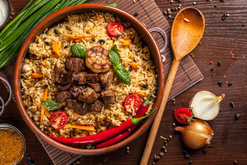 Uzbek restaurant concept, Uzbek food feast. Uzbek pilaf made from beef, lamb, chicken, in large earthenware, plate, next to vegetables. Copy space