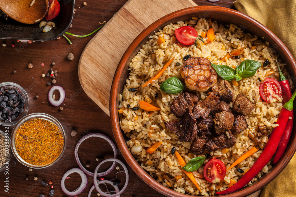 Uzbek restaurant concept, Uzbek food feast. Uzbek pilaf made from beef, lamb, chicken, in large earthenware, plate, next to vegetables. Copy space Uzbek restaurant concept, Uzbek food feast. Uzbek pilaf made from beef, lamb, chicken, in large earthenware, plate, next to vegetables. Copy space