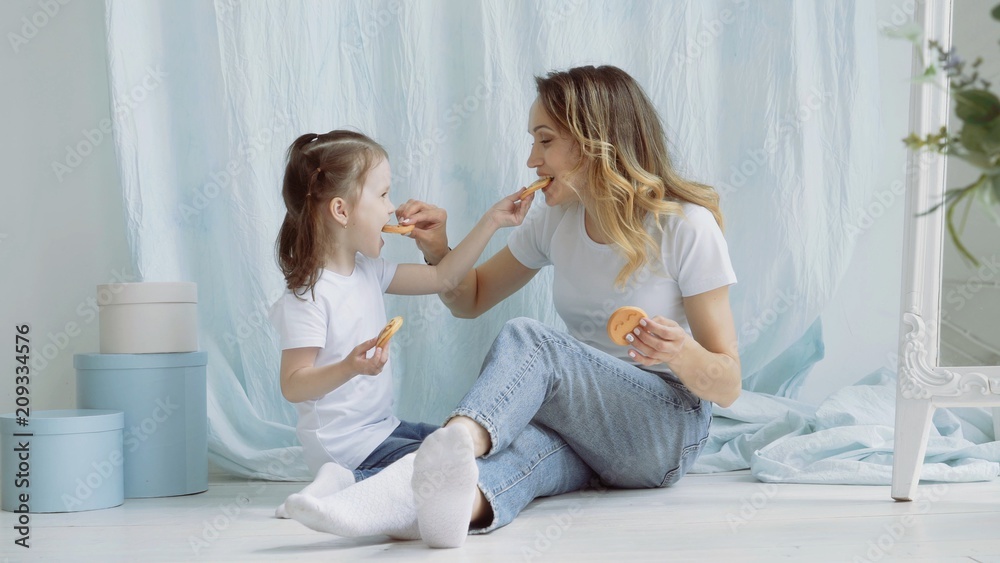 Obraz premium A young mother with a small daughter treat each other cookies.