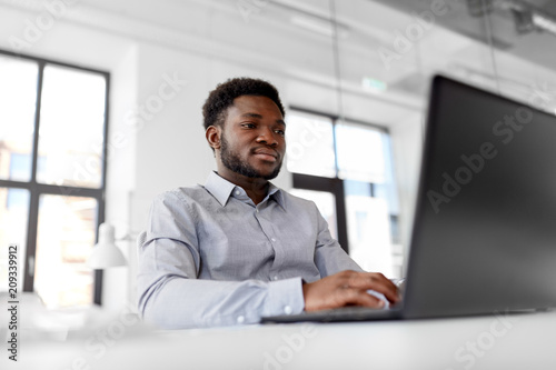 business, people and technology concept - african american businessman with laptop computer working at office