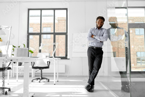 business and people concept - smiling african american businessman at office glass wall