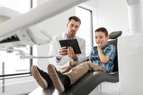 medicine, dentistry and healthcare concept - male dentist showing tablet pc computer to kid patient at dental clinic