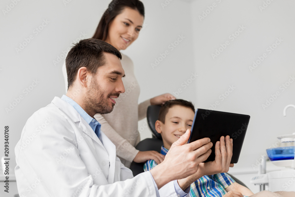 medicine, dentistry and healthcare concept - dentist showing tablet pc computer to kid patient and his mother at dental clinic medicine, dentistry and healthcare concept - dentist showing tablet pc computer to kid patient and his mother at dental clinic