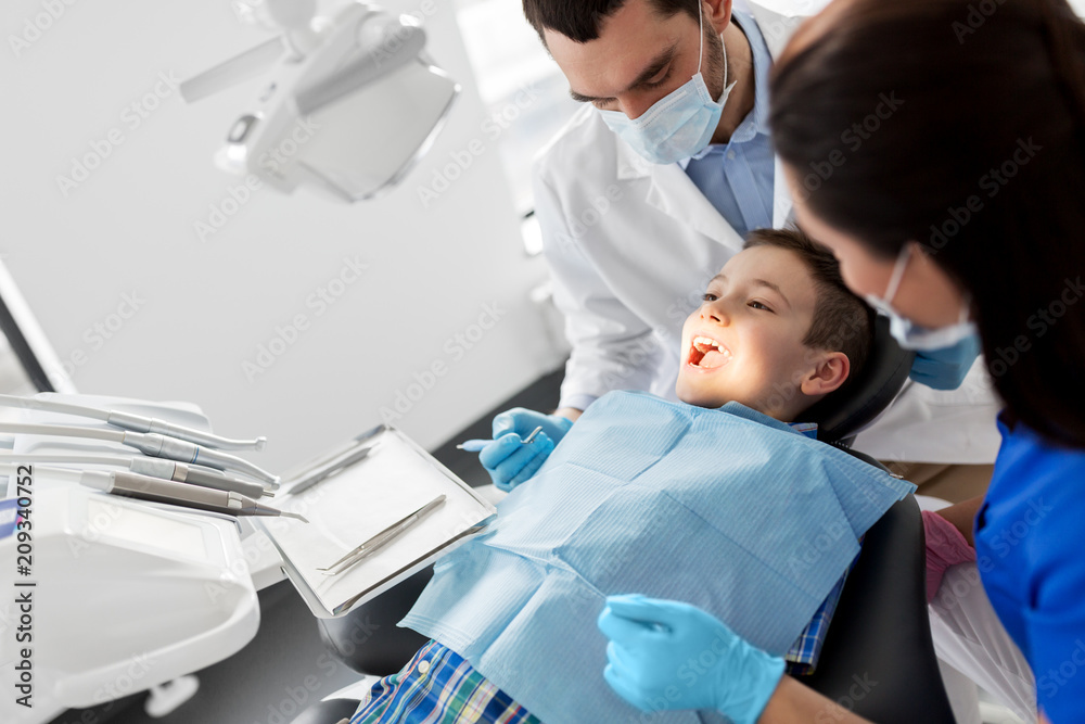 medicine, dentistry and healthcare concept - dentist with mouth mirror checking for kid patient teeth at dental clinic medicine, dentistry and healthcare concept - dentist with mouth mirror checking for kid patient teeth at dental clinic