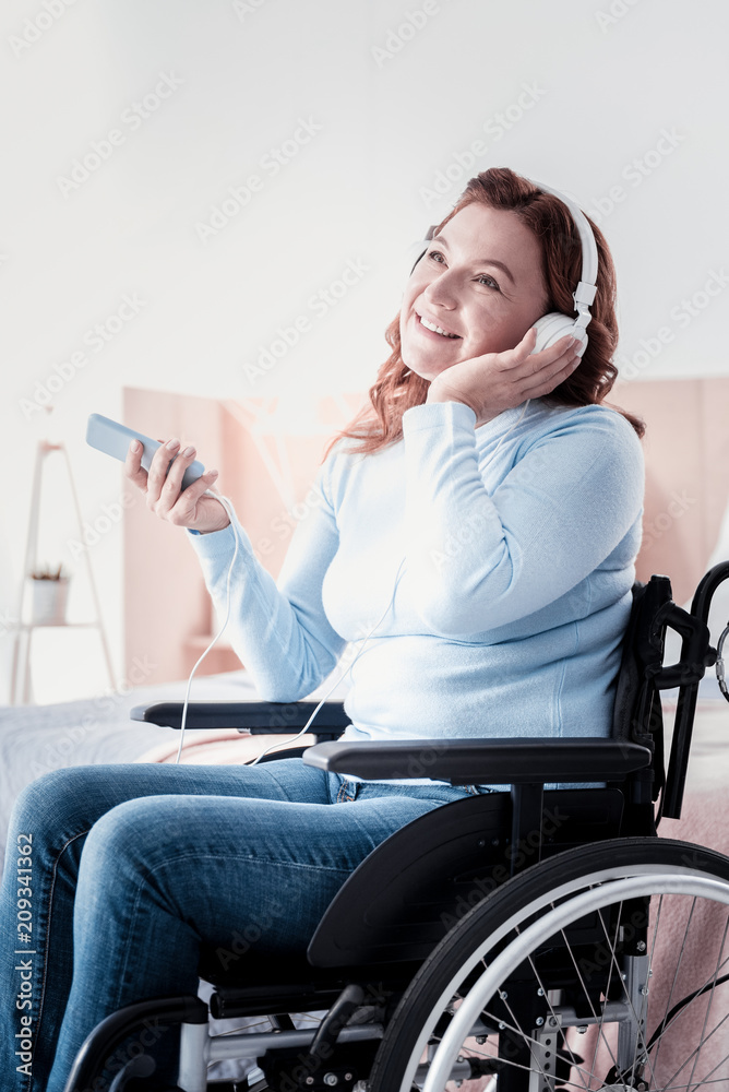 My weekend. Merry disabled woman sitting in a wheel chair and listening to music