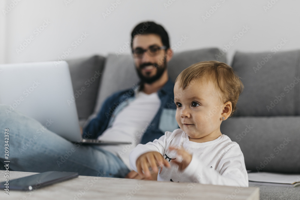 Father using laptop at home, daughter playing in the foreground Father using laptop at home, daughter playing in the foreground