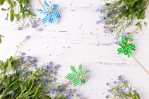 Summer background. Fresh blue forget-me-nots or myosotis flowers and bright windmills on white wooden background