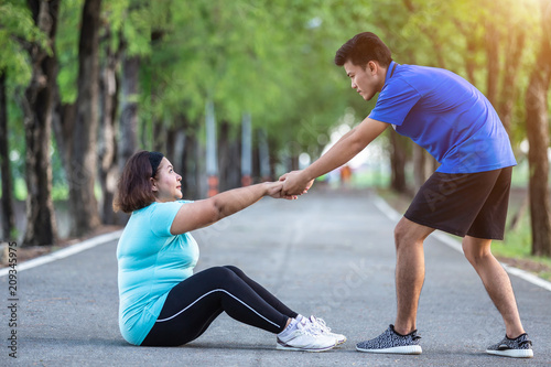 Asian man pulling hand of fat woman who tired and sitting on ground
