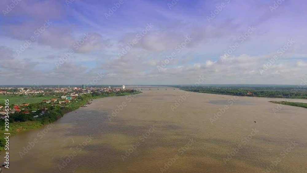 aerial drone shot : fly back revealing villages along the riverside with the shadow of clouds passing over the Mekong River. Town and bridge in the background aerial drone shot : fly back revealing villages along the riverside with the shadow of clouds passing over the Mekong River. Town and bridge in the background