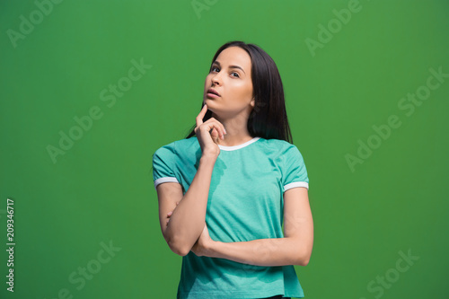 Let me think. Doubtful pensive woman with thoughtful expression making choice against grreen background