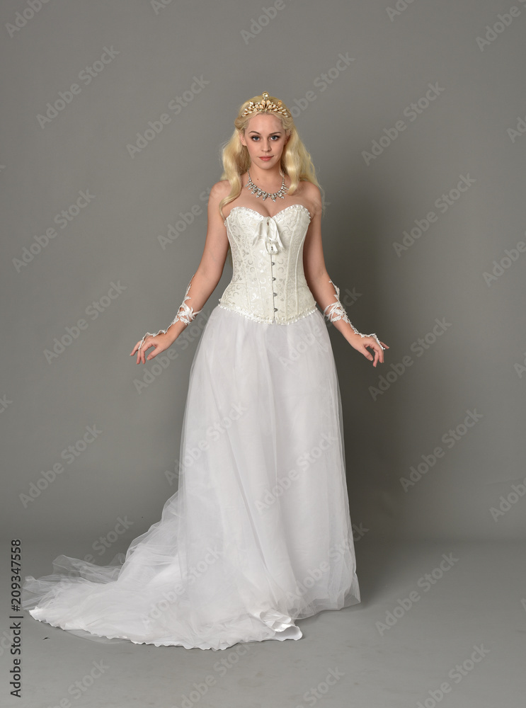 full length portrait of blonde girl wearing white corset gown. standing pose on grey studio background. full length portrait of blonde girl wearing white corset gown. standing pose on grey studio background.