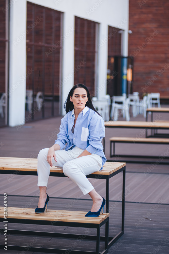 Fototapeta premium A beautiful woman in a shirt and pants sits on a balcony of a building.