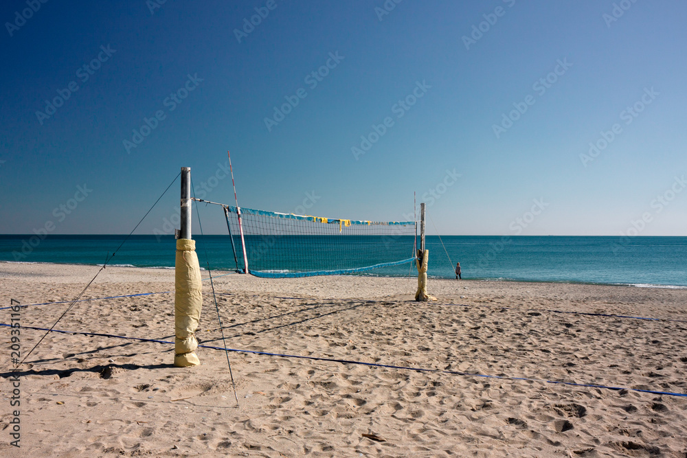 View on a deserted beach with a volleyball court, a person walks by the sea.