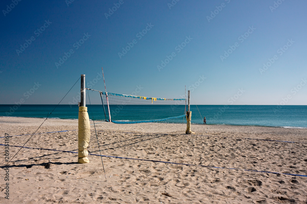 View on a deserted beach with a volleyball court, a person walks by the sea. View on a deserted beach with a volleyball court, a person walks by the sea.