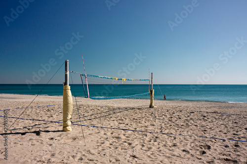 View on a deserted beach with a volleyball court  a person walks by the sea.