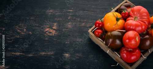 Assortment of tomatoes in a wooden box. Fresh vegetables. On a black wooden background. Top view. Copy space.